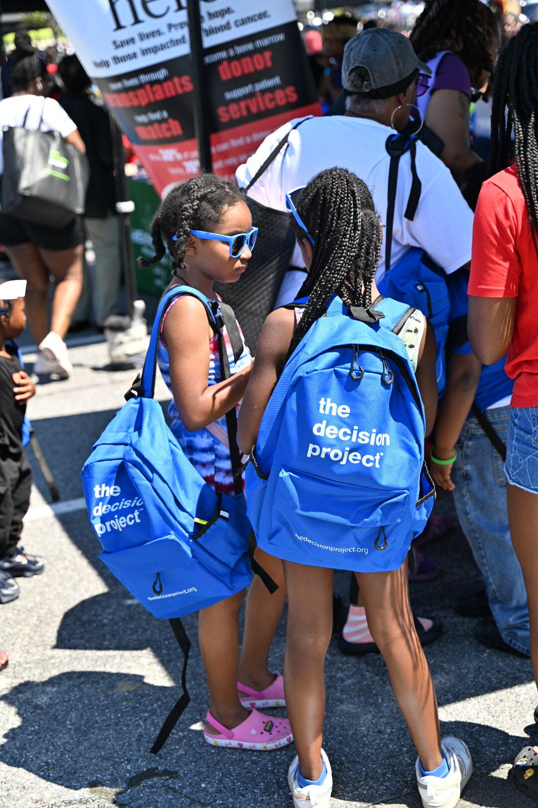 Two children are standing together at an Infinite Legacy Block Party with The Decision Project backpacks.