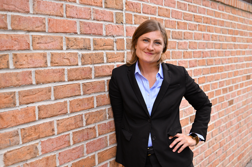 Senior Director, Hospital Services and Organ Family Services, Emily Cullen, leans against a brick wall outside of Infinite Legacy's office smiling.
