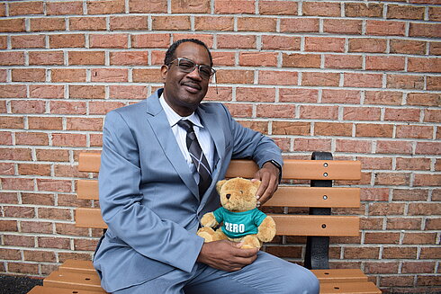 Vice President and Chief Business Development Officer, Kenneth Boyd sits on a bench holding a hero heart teddy bear to support organ, eye and tissue donation.