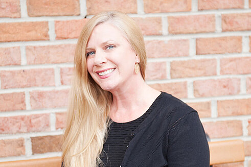 Headshot of Vice President and Chief Clinical Officer, Debbi McRann smiling in front of Infinite Legacy's office.