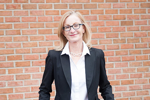 Vice President of External Affairs and Education, Karen Kennedy, stands in front of Infinite Legacy's office smiling.